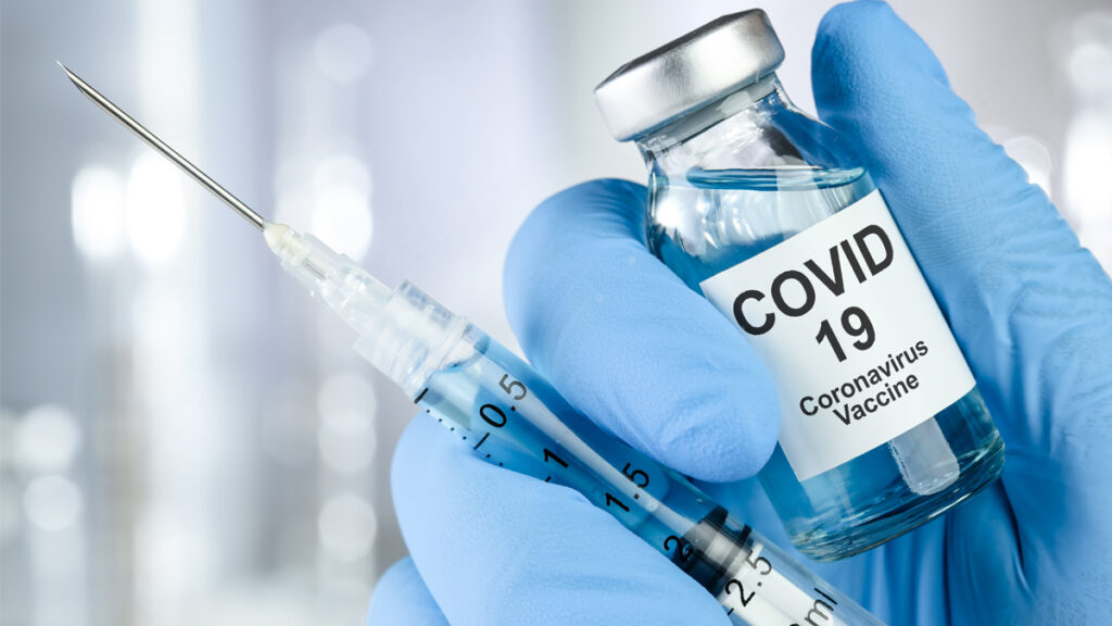 Healthcare cure concept with a hand in blue medical gloves holding Coronavirus, Covid 19 virus, vaccine vial.