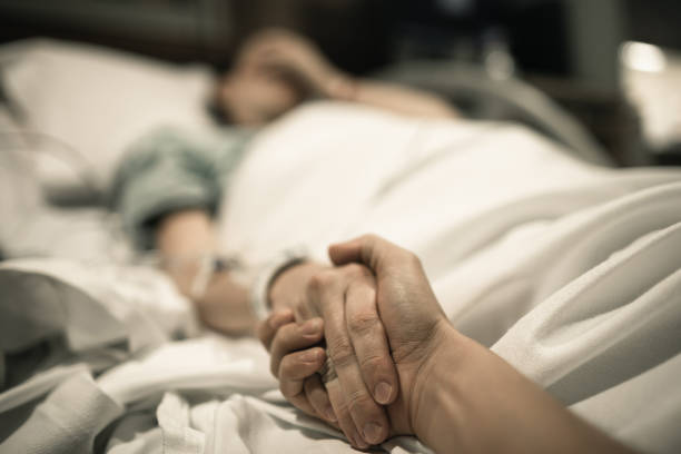 Sick woman lying in hospital bed with hand being held by love one. Family lines and medical tragedy concept.